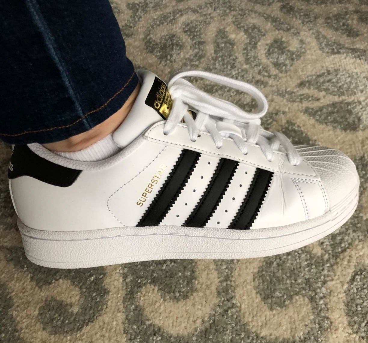 A reviewer wearing the Adidas Originals Superstar sneaker in white with black accents