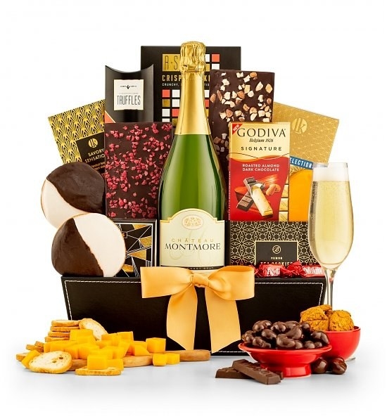 A gift basket full of various chocolates, cookies, crackers, and a champagne bottle