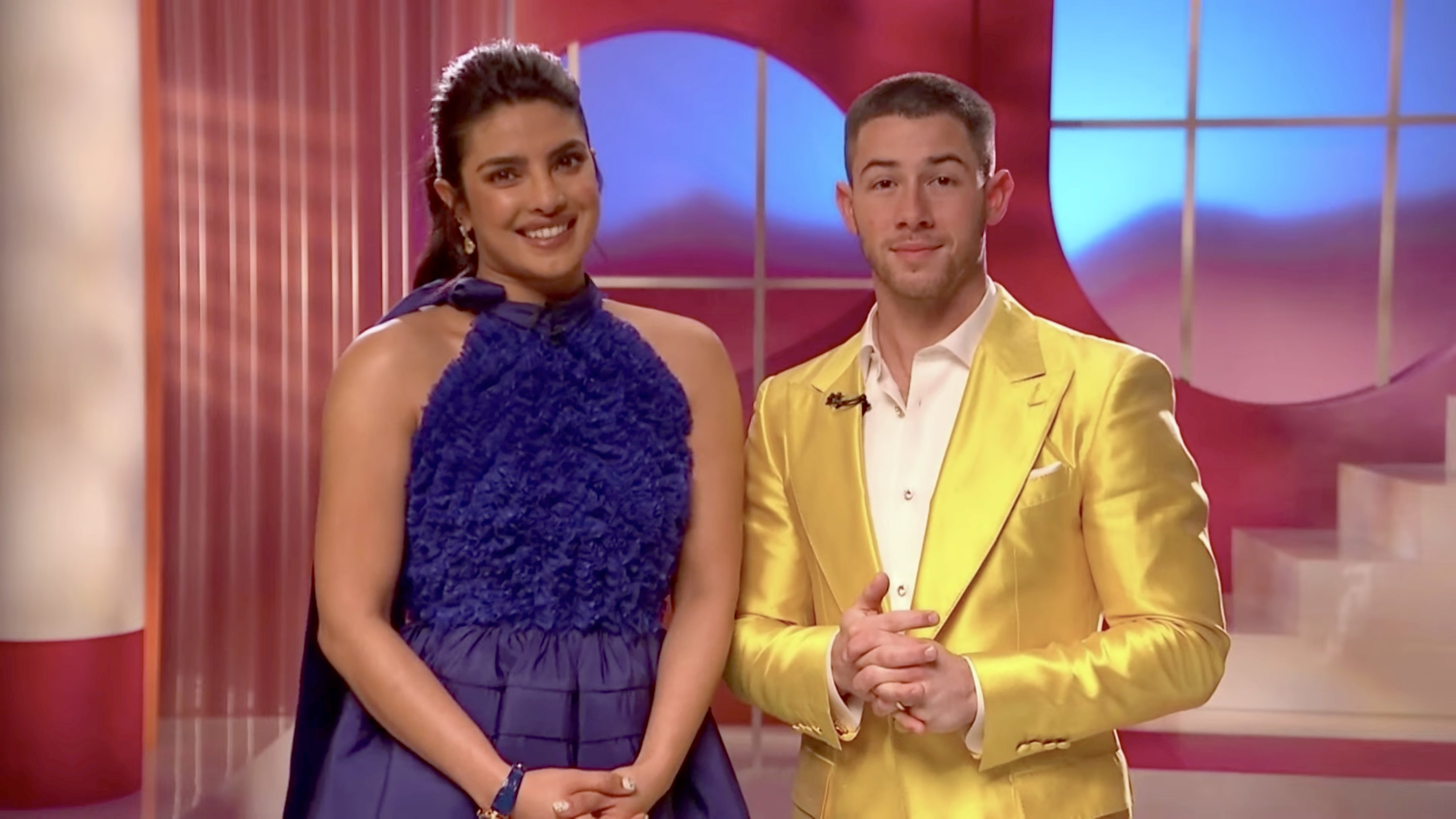Priyanka in a halter dress standing next to Nick who&#x27;s wearing a metallic colored suit
