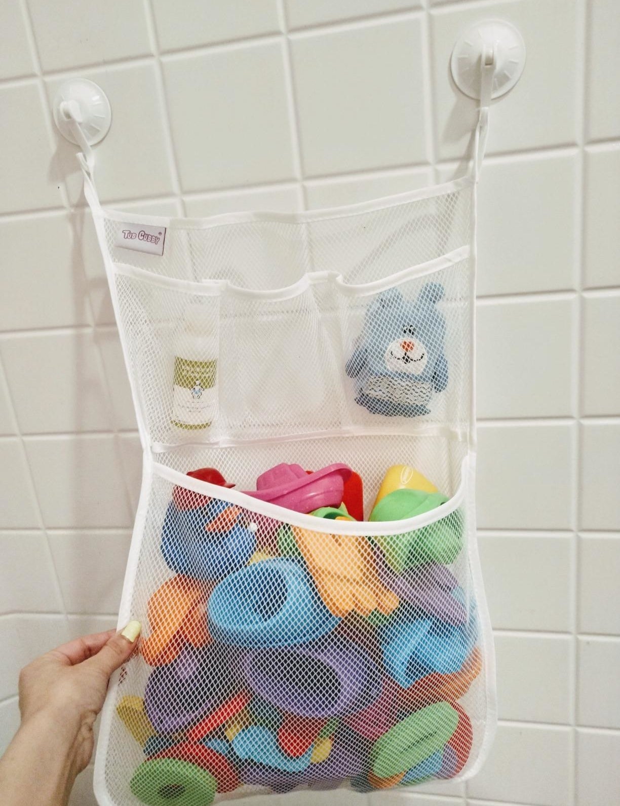 a reviewer photo of a white mesh organizer with one big pocket and three small pockets mounted with two suction cup hooks