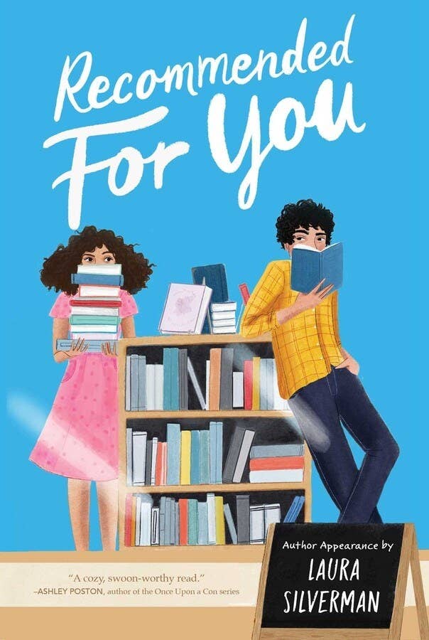 Blue cover. Two white teenagers, a girl in a pink dress and a boy in a yellow button-up shirt and jeans, stand next to a full bookcase. Title reads: Recommended for You. A blackboard sign reads: Author Appearance by Laura Silverman.