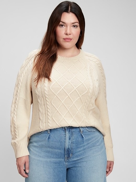 model wearing a cream-colored cable knit sweater with light blue jeans