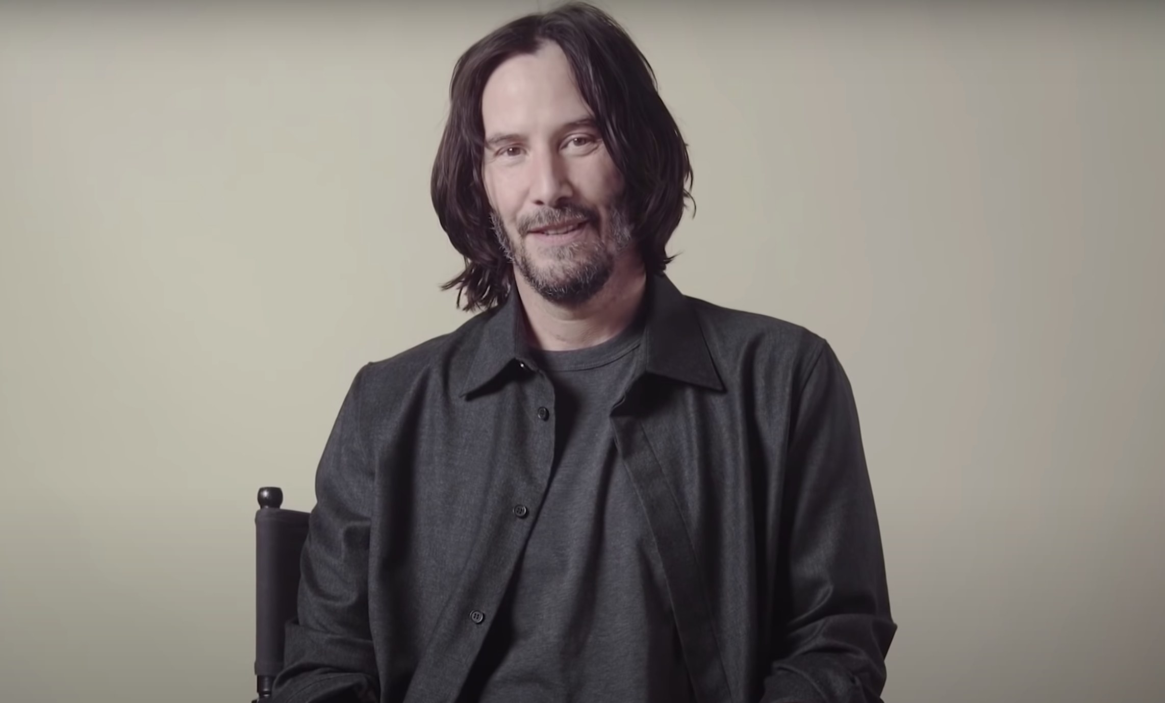 Keanu sits in a chair for the interview in front of a plain backdrop