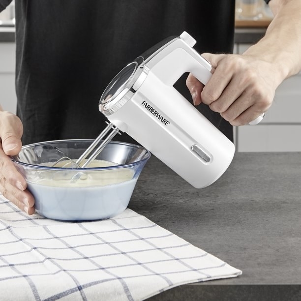 A person using the white hand mixer to beat cream.