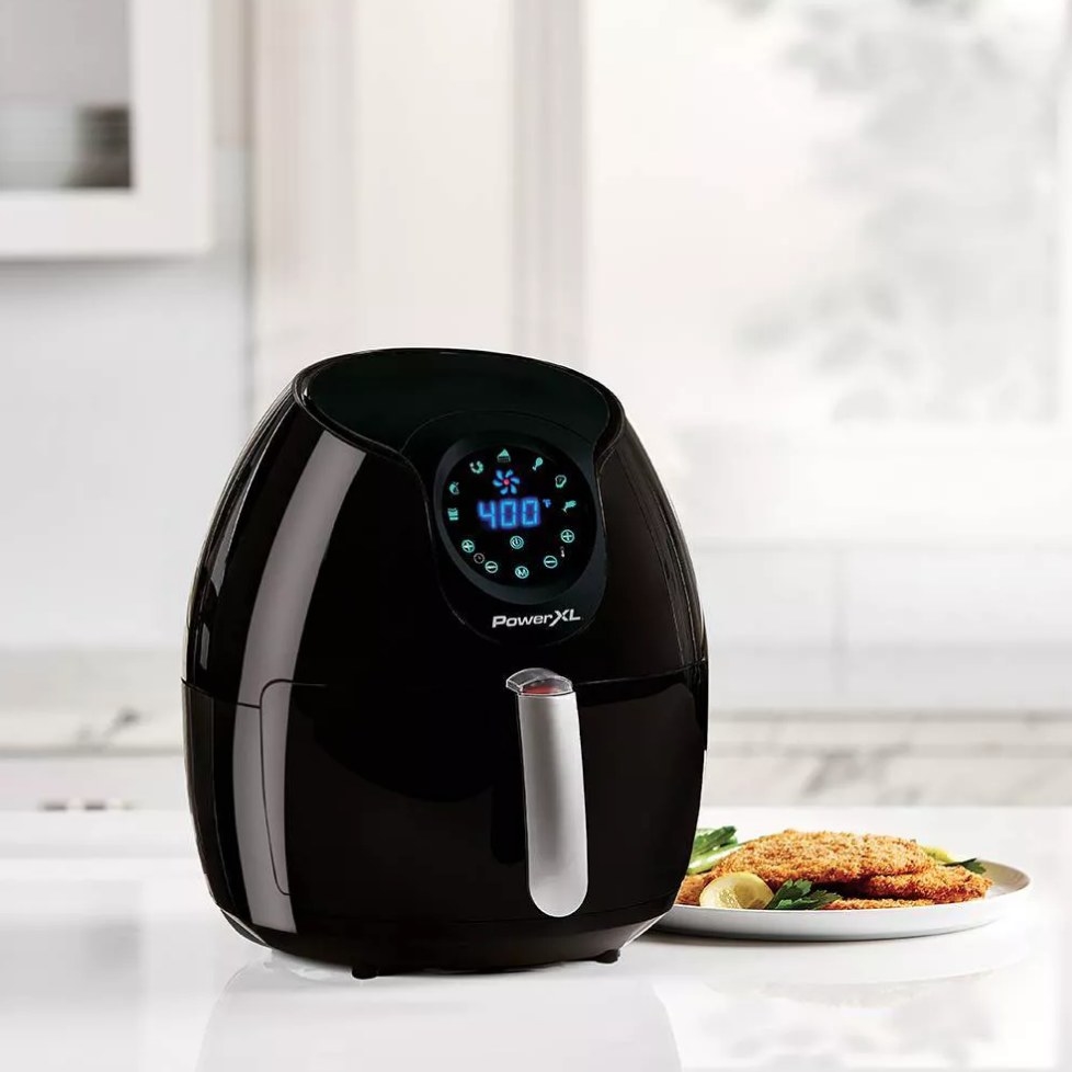 Black air fryer next to plate of food on counter