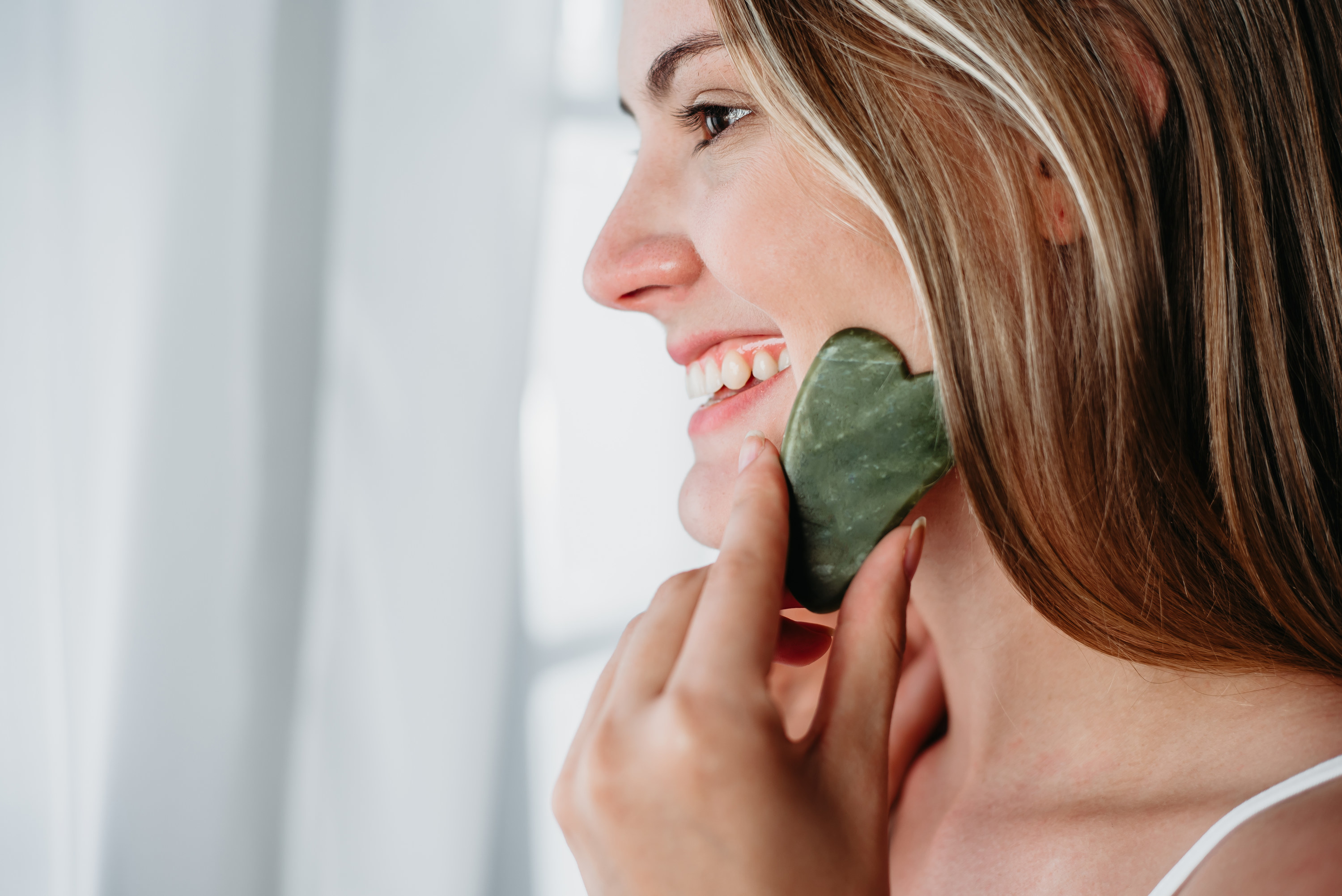 A woman using a gua sha stone on her face to massage it