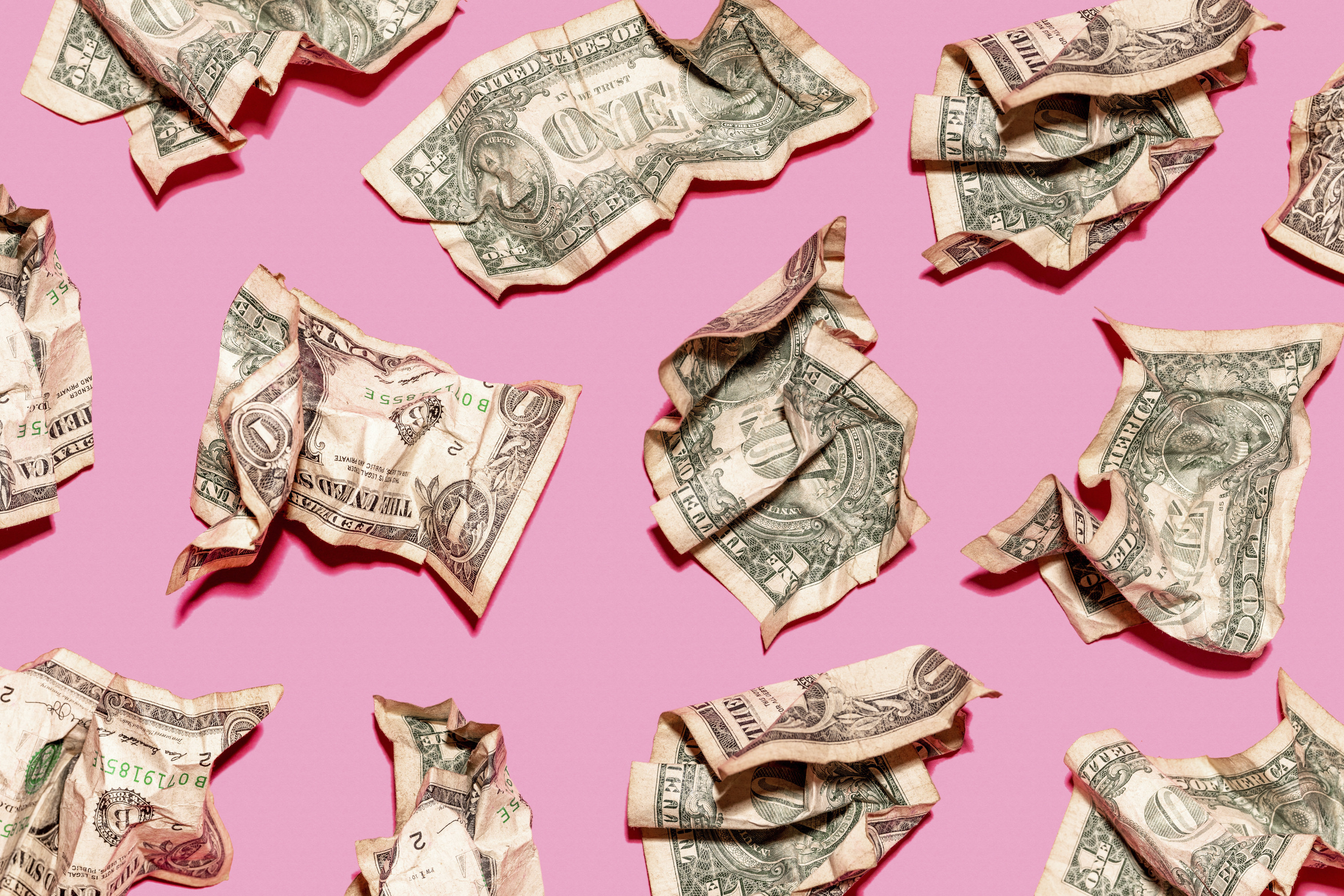 Dollar bills crumbled up against a pink background
