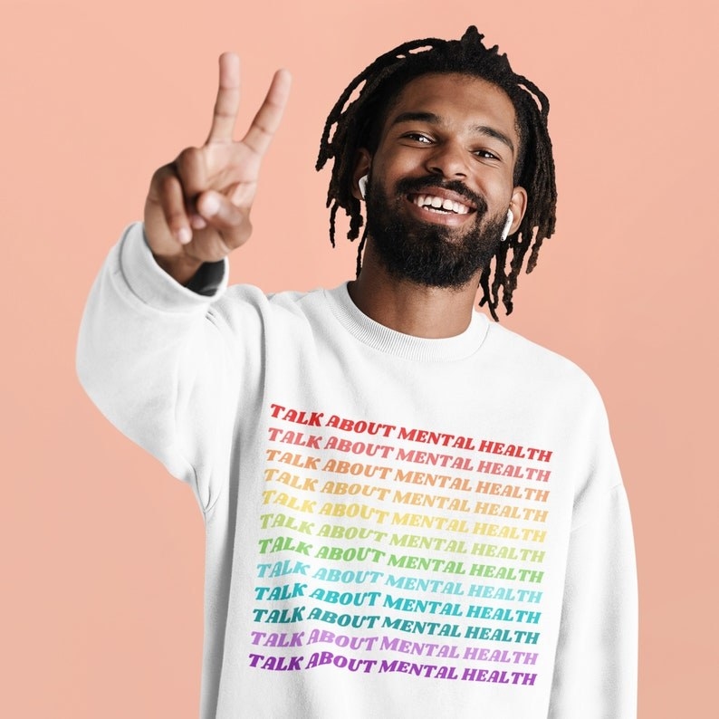 model wearing the white crew neck sweat shirt that says "talk about mental health" in rainbow letting