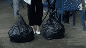A woman throwing down two black trash bags onto the street