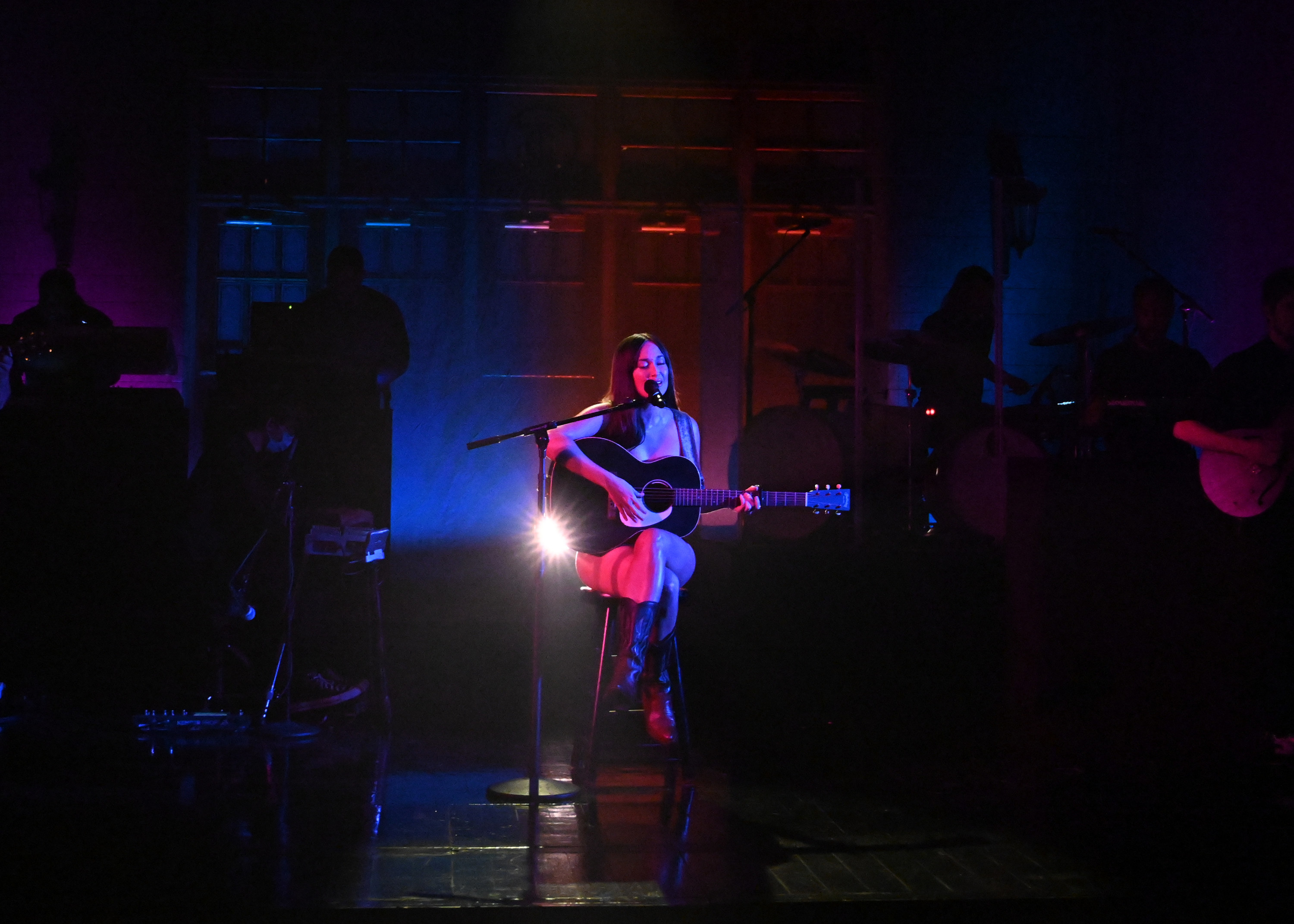 Kacey is naked while while sitting on a stool being covered up by a guitar