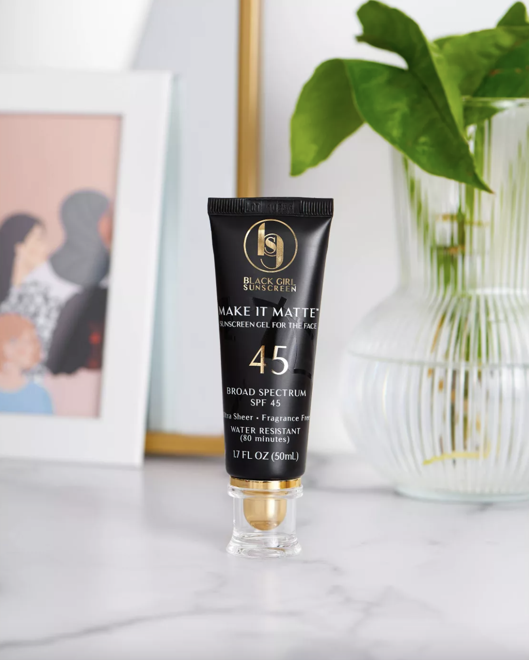 A tube of black girl sunscreen sitting on a counter in front of a plant and picture frame