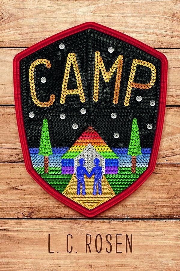Wooden background featuring a sequined patch. On the patch there is a rainbow house and two blue figures holding hands. Title reads: &quot;Camp.&quot;