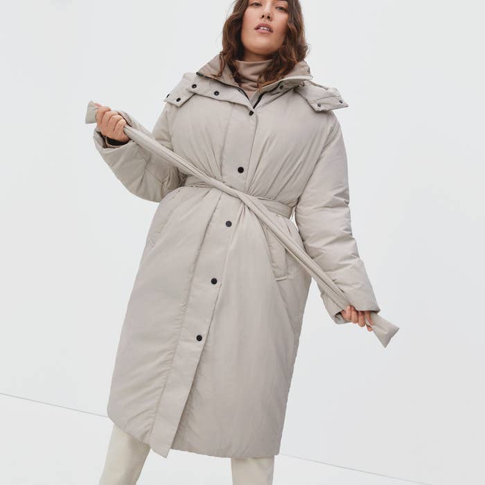 Model wearing the white knee-length coat and tieing the waist