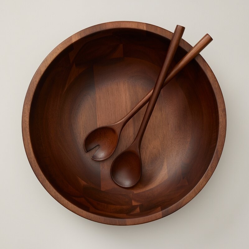 a pair of slim wooden salad servers inside a matching bowl