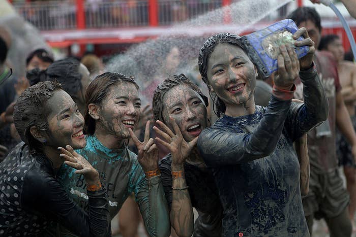 Women smiling and taking a selfie while celebrating The Mud Festival of South Korea