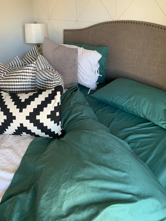 reviewer photo of the sheets in green with black and white throw pillows on the bed
