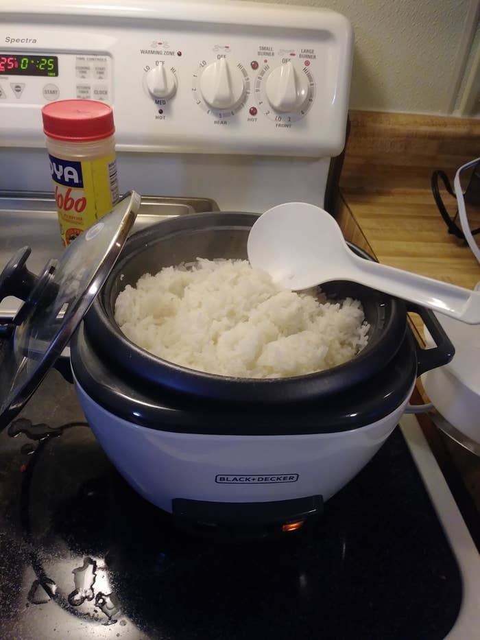 the rice cooker on a stove with white rice in it