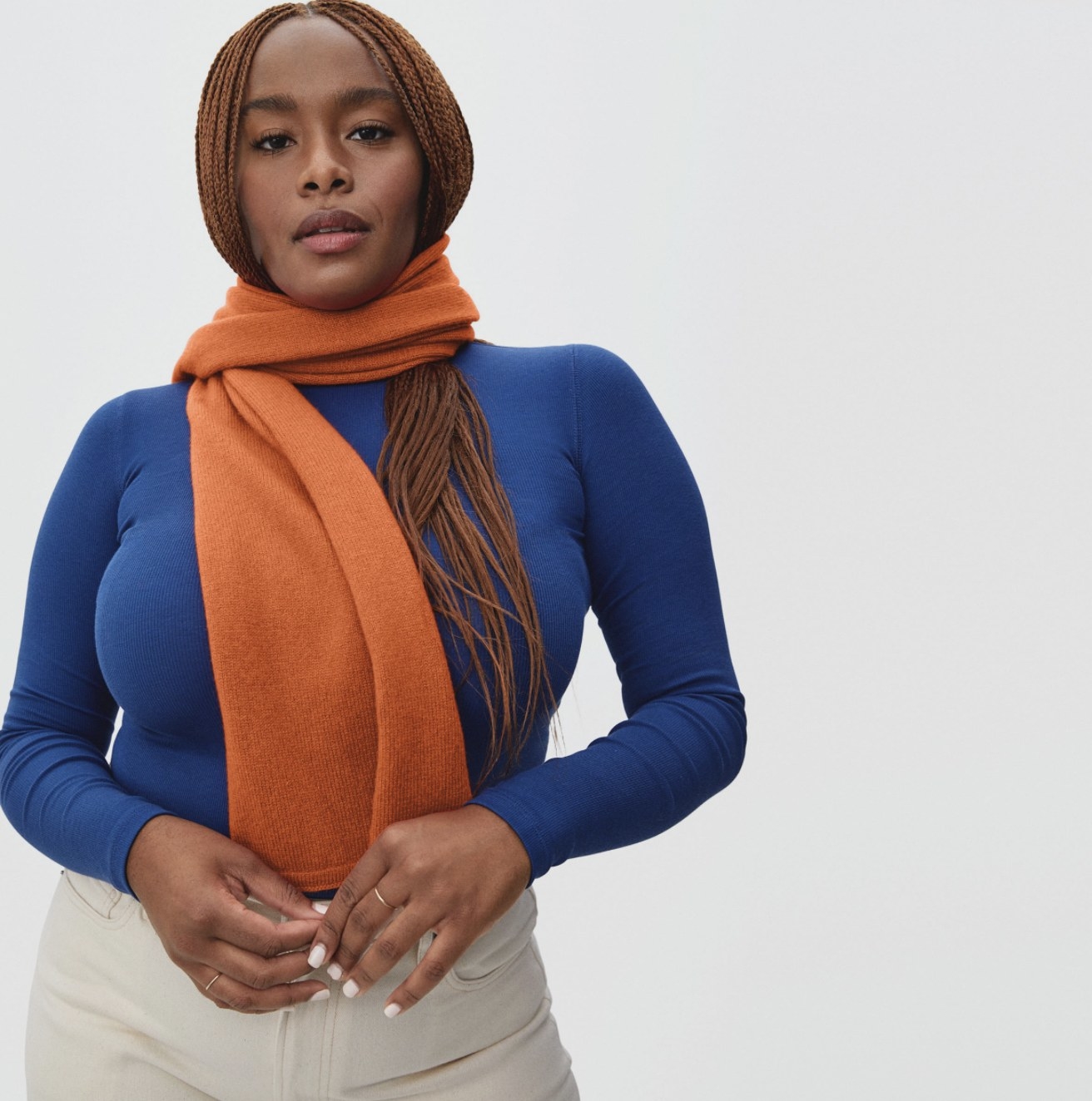 Model wearing the orange scarf wrapped around her neck with a blue long-sleeve