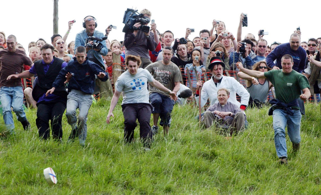 A group of participants racing down a grassy hill, chasing a rolled block of cheese in celebration of the country&#x27;s Cheese Rolling Festival