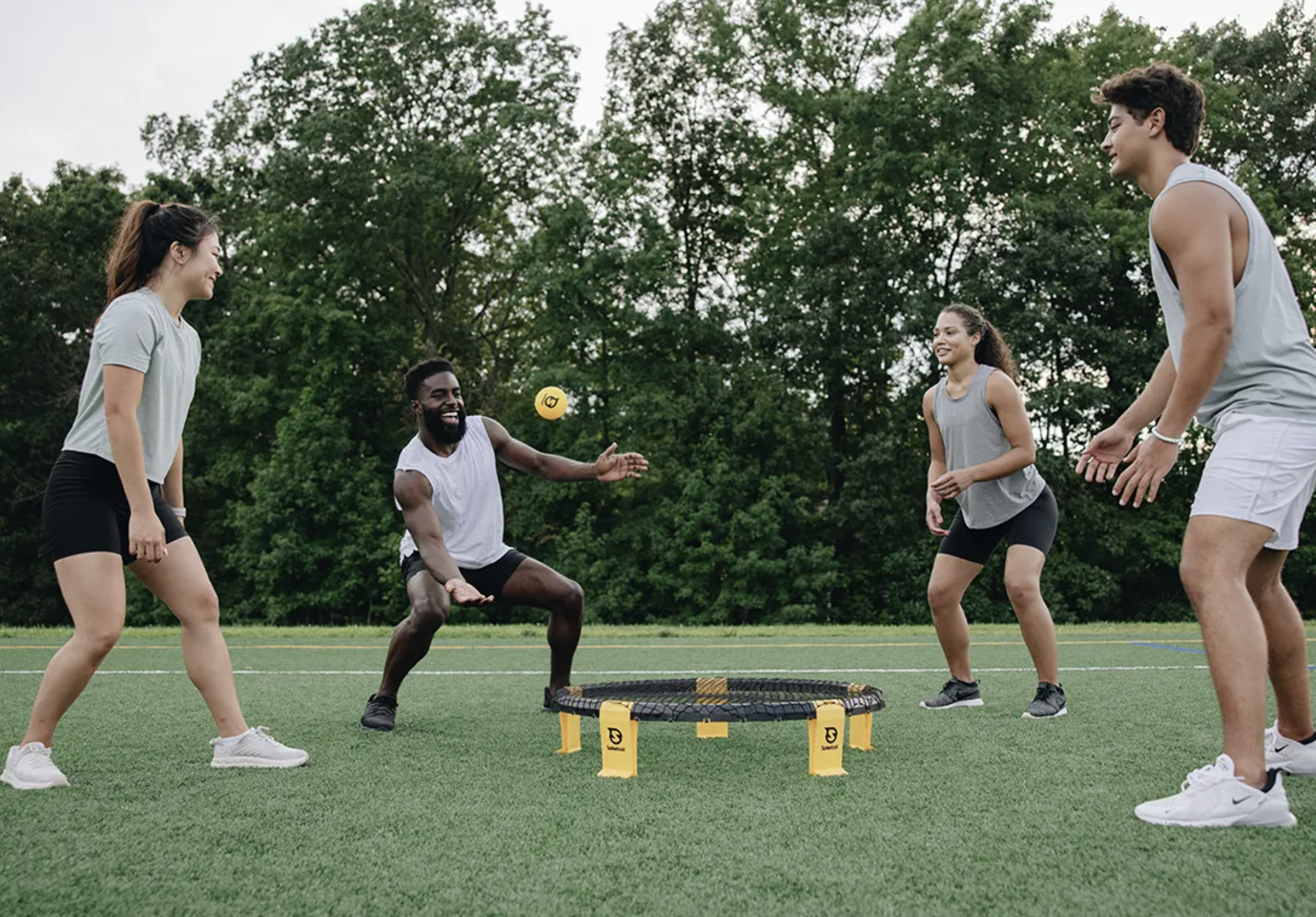 Four people playing Spikeball on a lawn