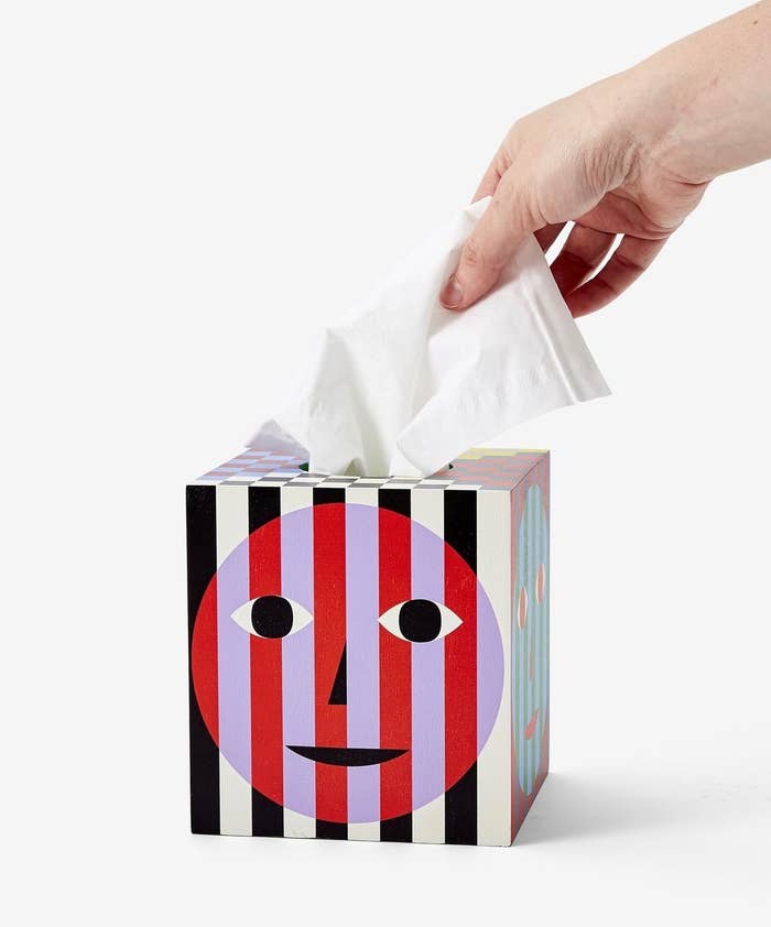 a model grabbing a tissue from the tissue box cover which has an abstract face