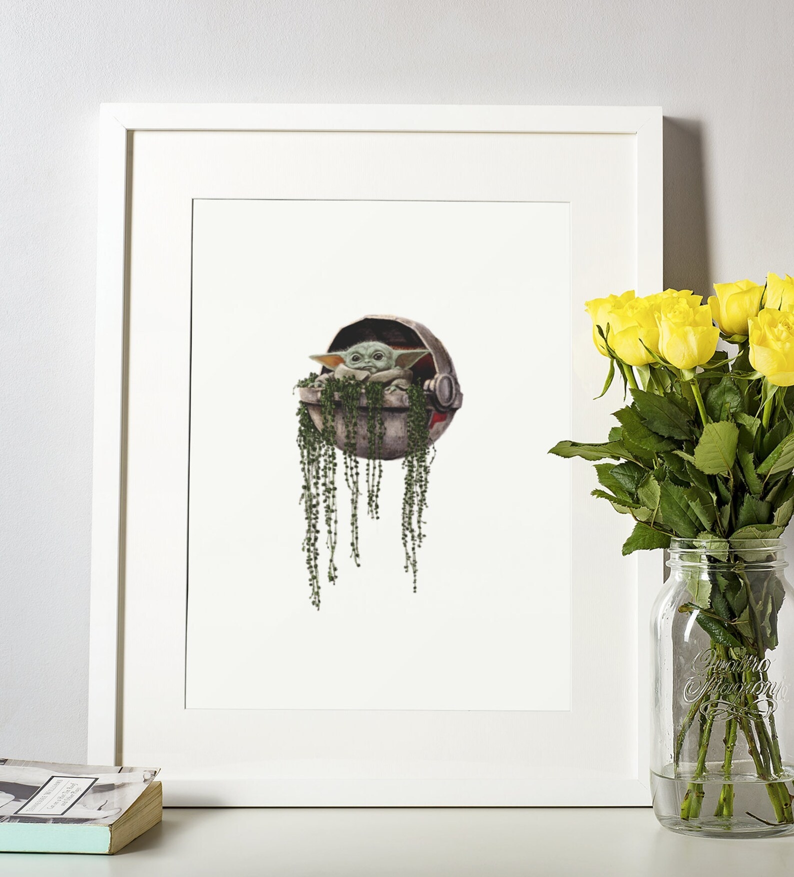 A framed baby Yoda print next to a vase of fresh flowers