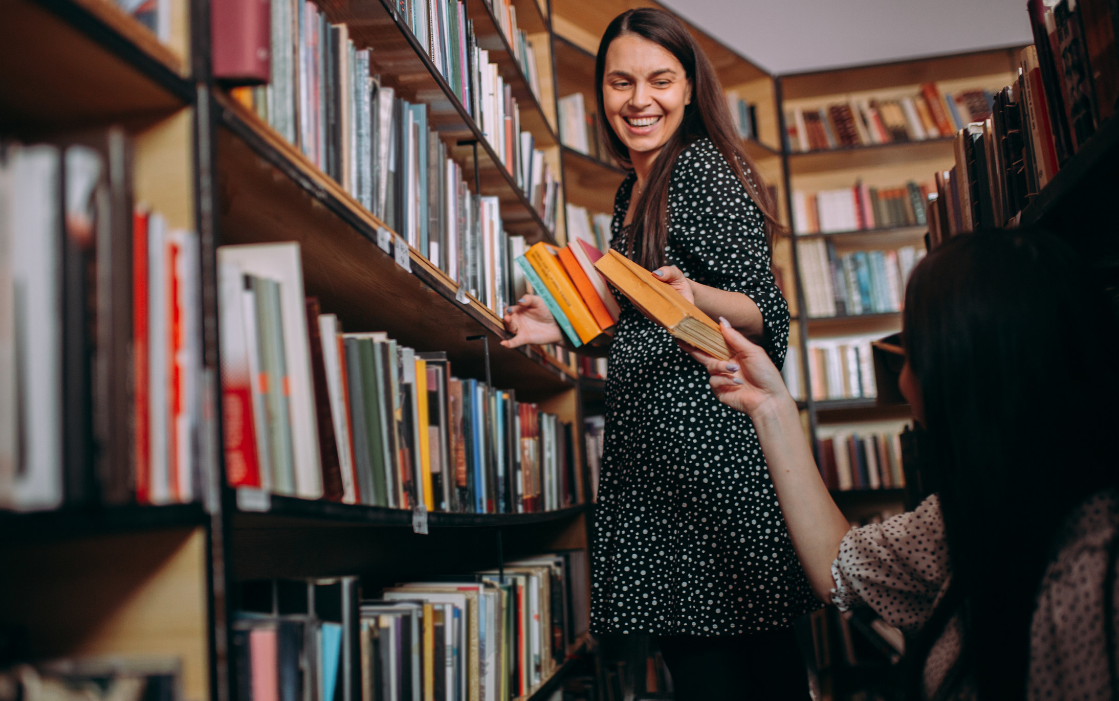 A librarian hands a book from a shelf to a patron