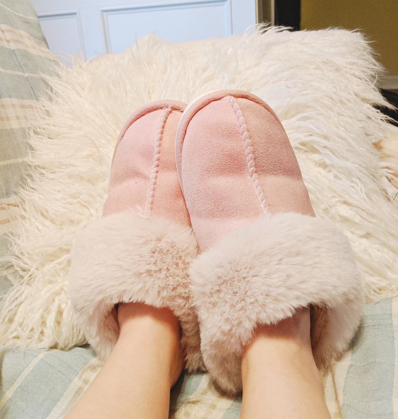 A reviewer&#x27;s photo of them wearing a pair of snuggly memory foam slippers with faux fur around the edges.