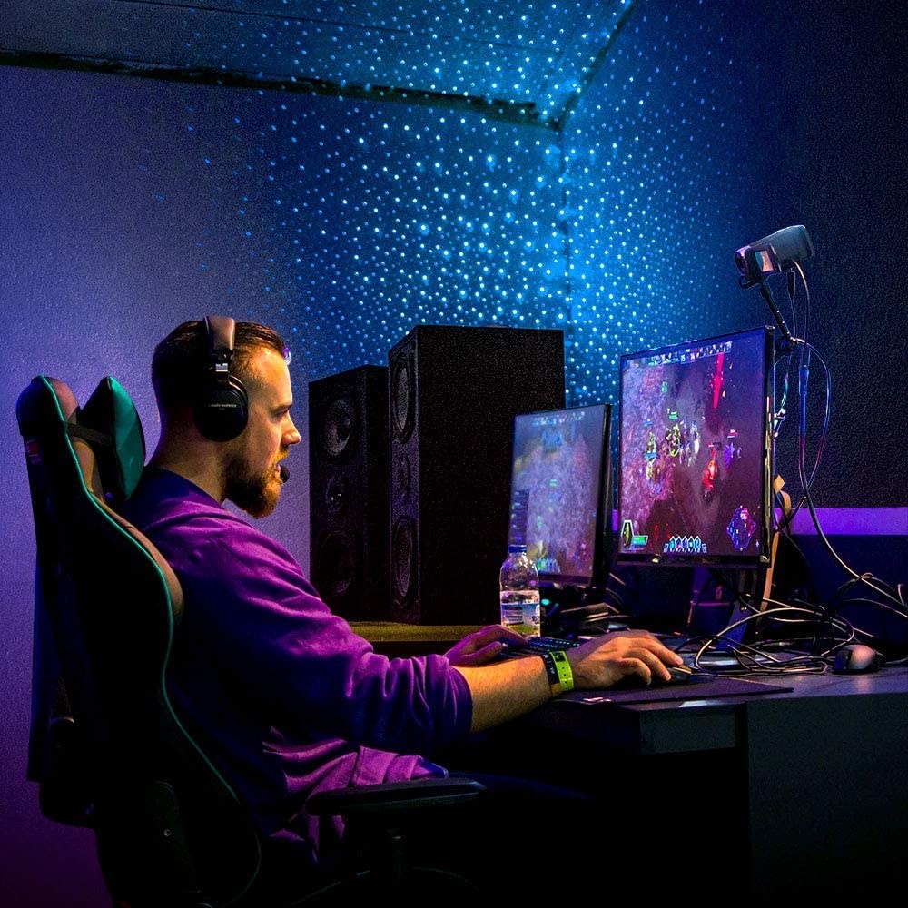 a person gaming on their computer with the starlight projector shooting lights on their dark walls
