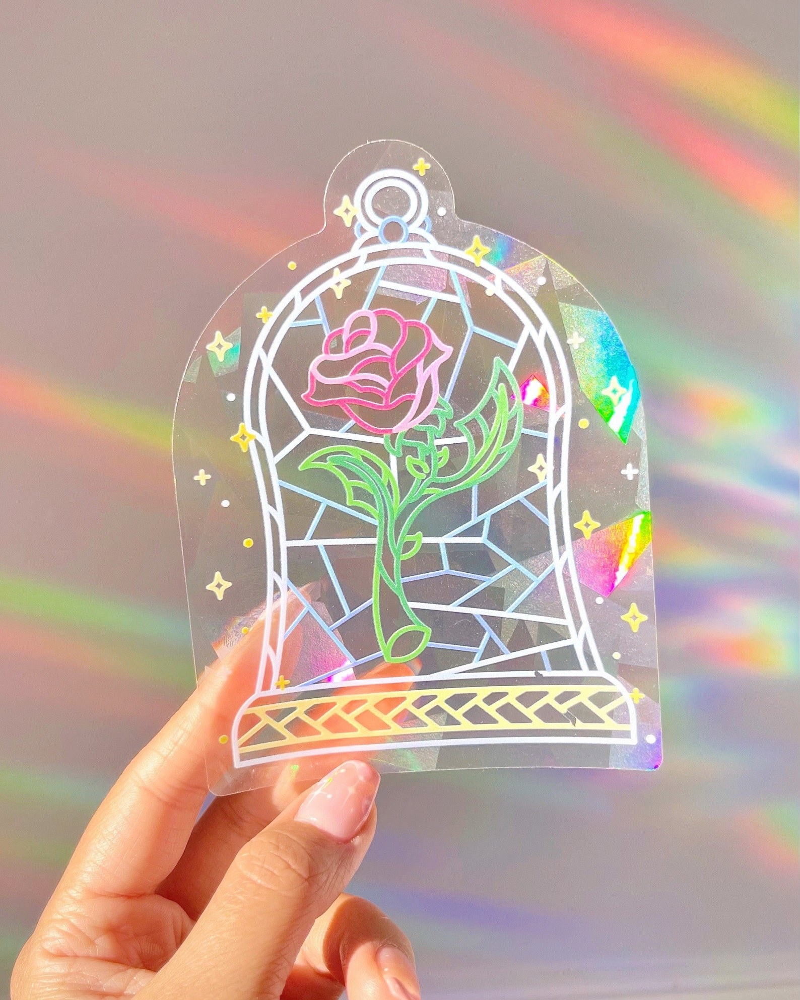 person holding up a sun catcher that has the enchanted rose from beauty and the beast on it