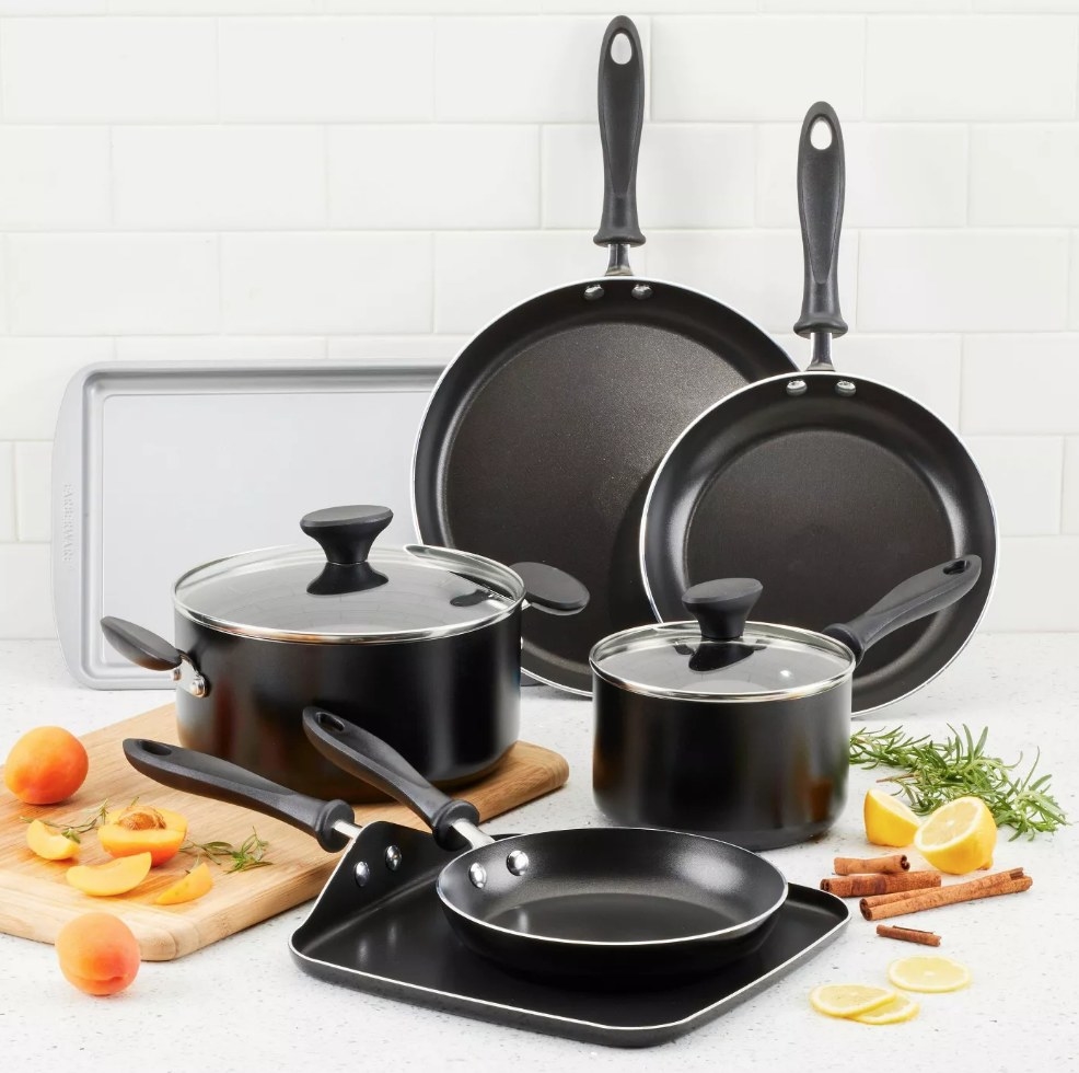 Left to right: black saucepan with lid on cutting board, cookie sheet behind it, two frying pants next to cookie sheet, small saucepan with lid on right, griddle and small frying pan in middle