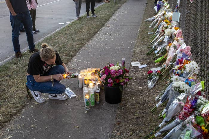 Woman kneeling at a memorial with candles and flowers on the street