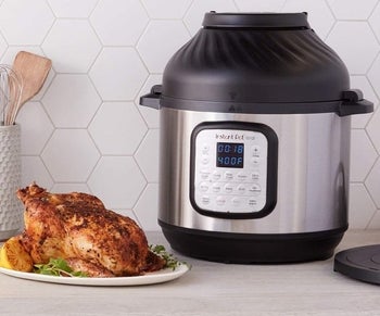 Silver and black instant pot with control panel next to a cooked chicken