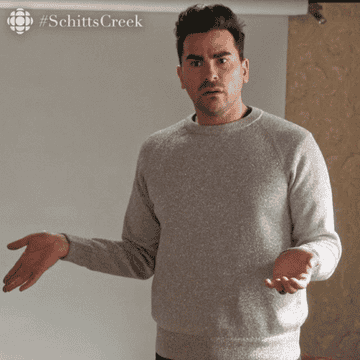 Man wearing a grey jumper with his arms out pulling a confused face.
