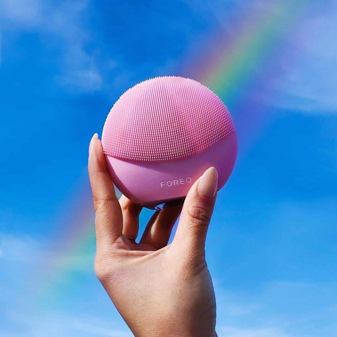 a person holding up the foreo brush against a clear sky
