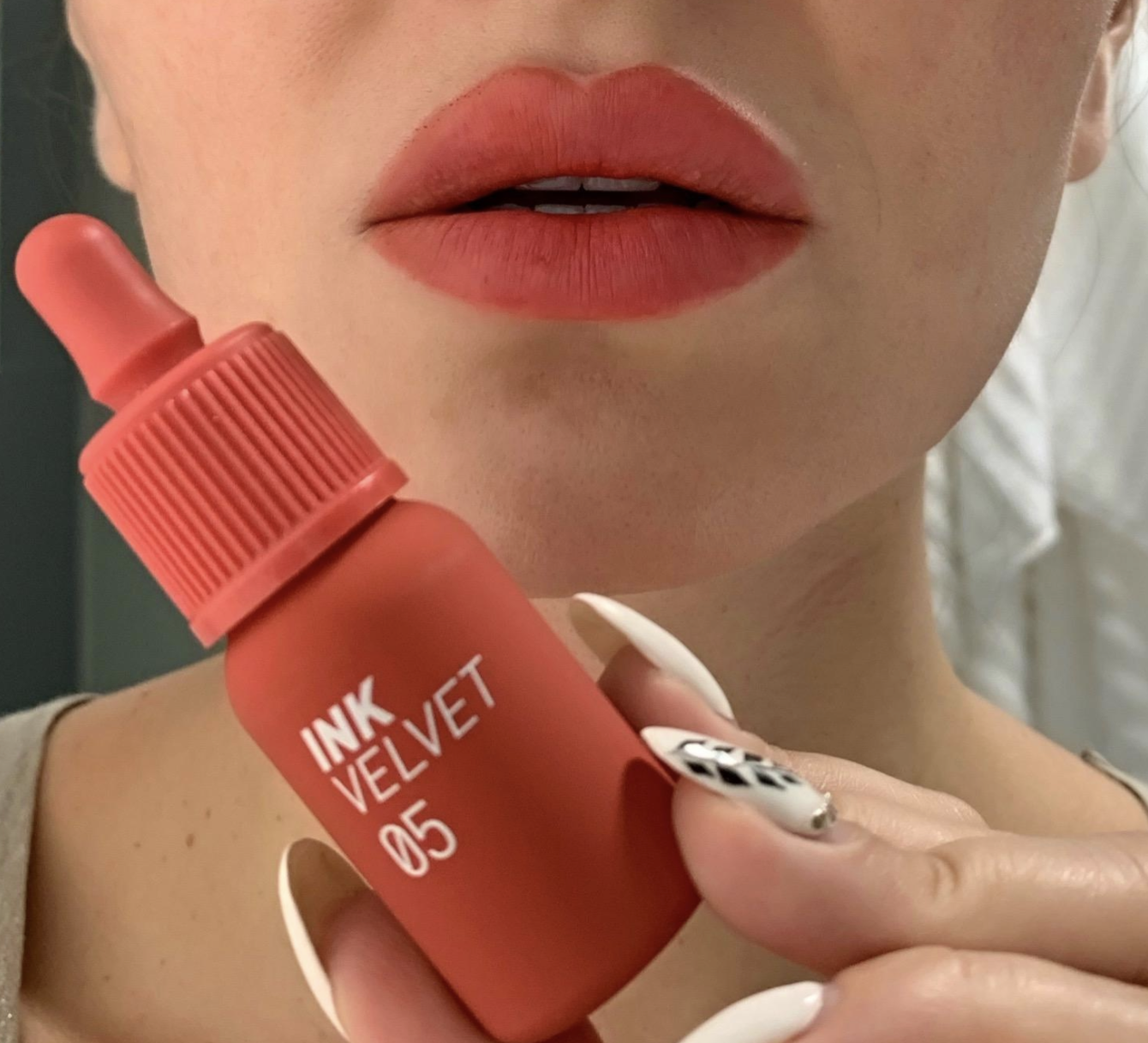 reviewer holding the tube of lipstick next to their lips to show the color