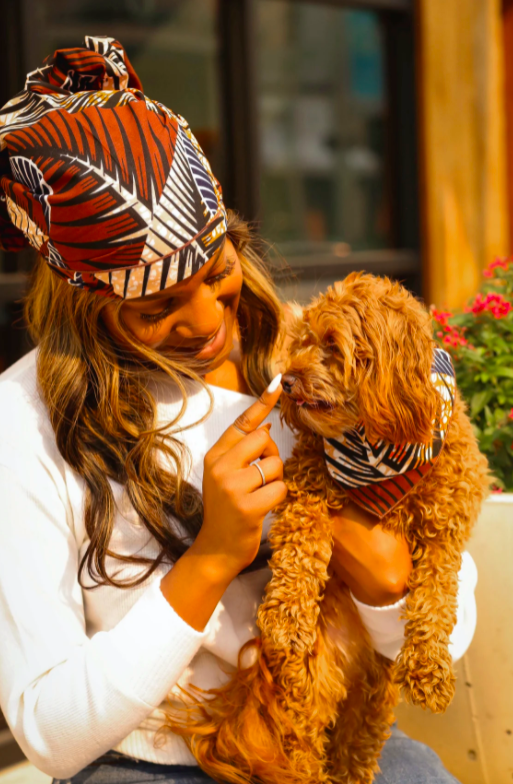 model holding their dog and the model is wearing an African print bandana while the dog is wearing a matching one around their neck