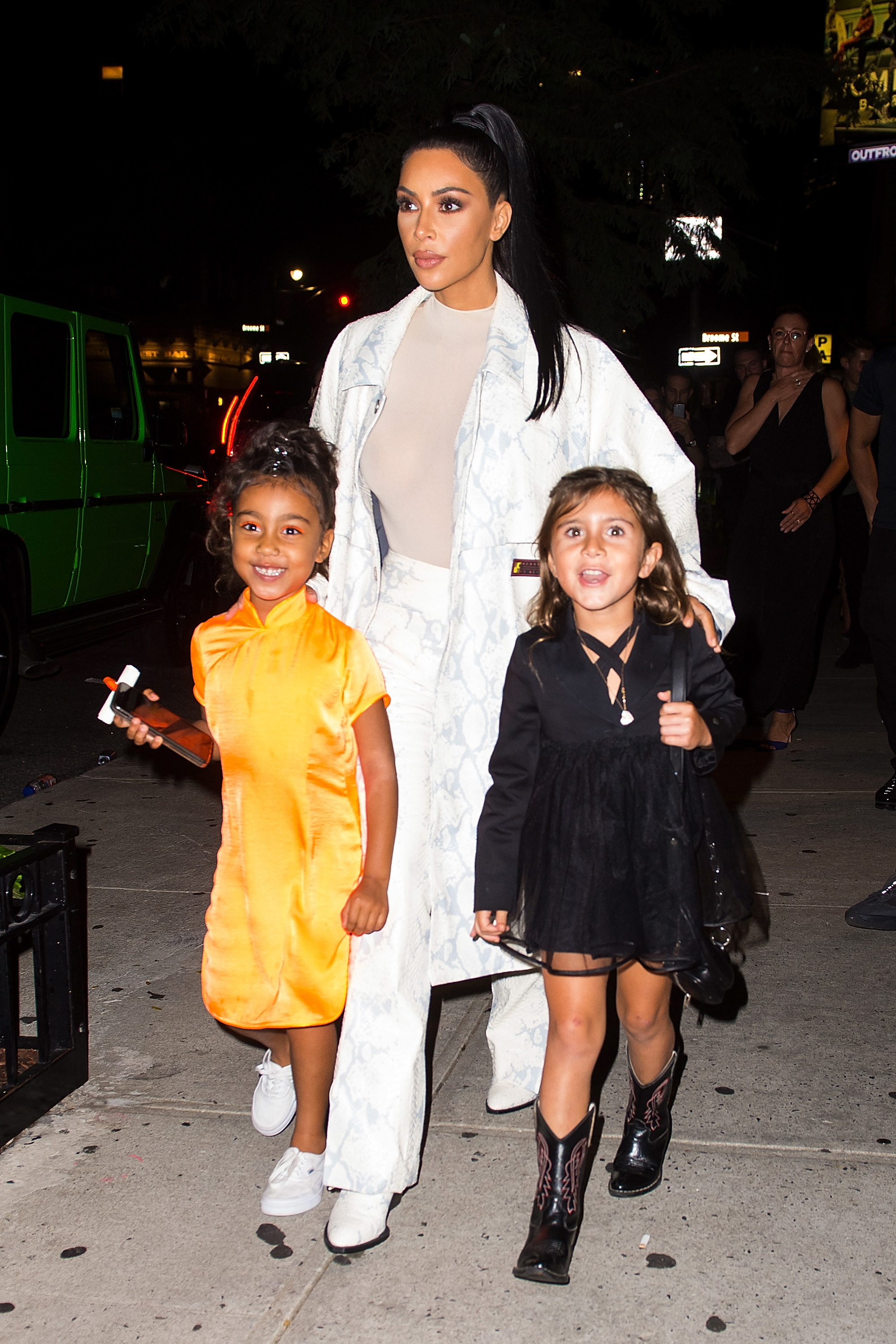 Kim walking down a sidewalk at night with North and Penelope