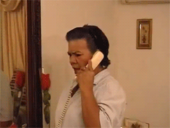 Woman on landline phone turns to the camera and gasps