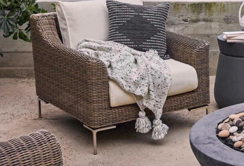 wicker otudoor chair with arms, a back and bottom cushion, a throw blanket, and a pillow in it