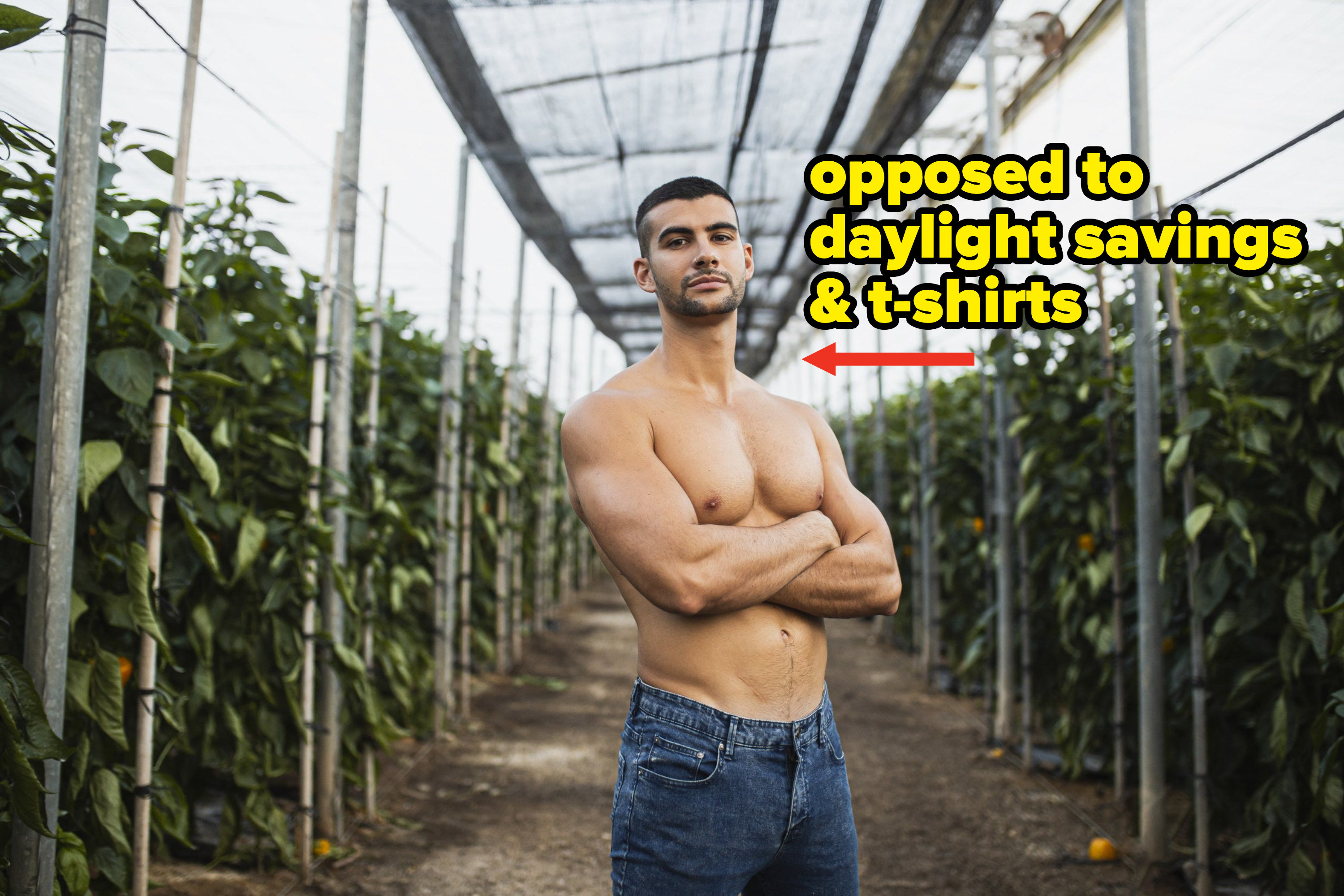 Young shirtless man standing with arms crossed at alley amid plants in greenhouse