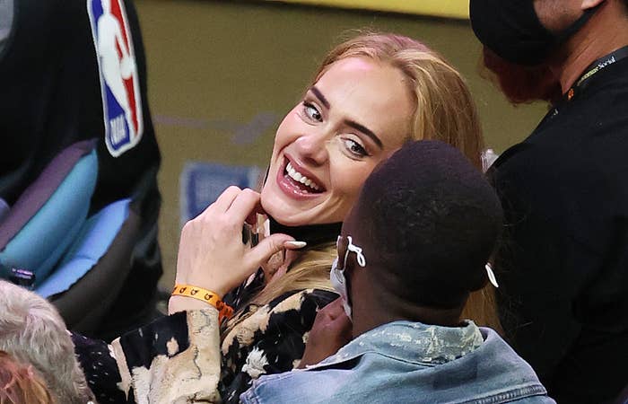 Adele laughing as she looks at someone behind her at an NBA basketball game
