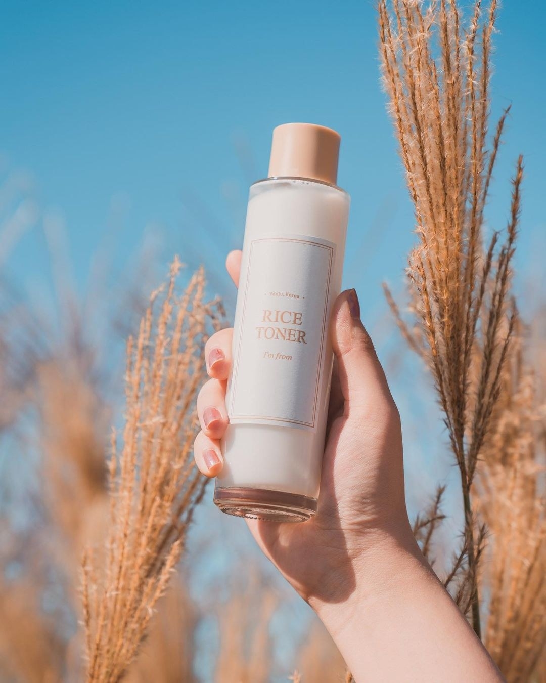 someone holding up a bottle of the toner in a rice field