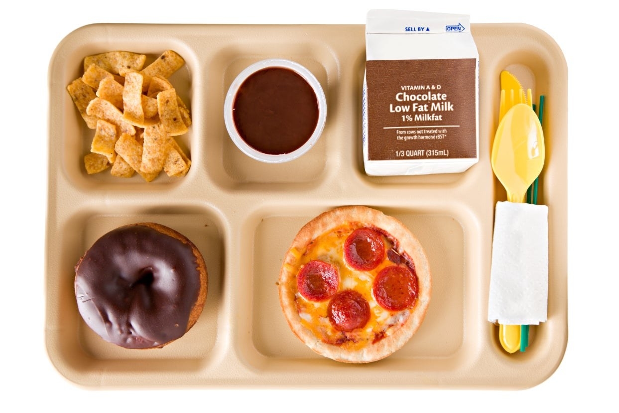 A school lunch tray with fritos, a donut, low-fat chocolate milk, and a mini pepperoni pizza