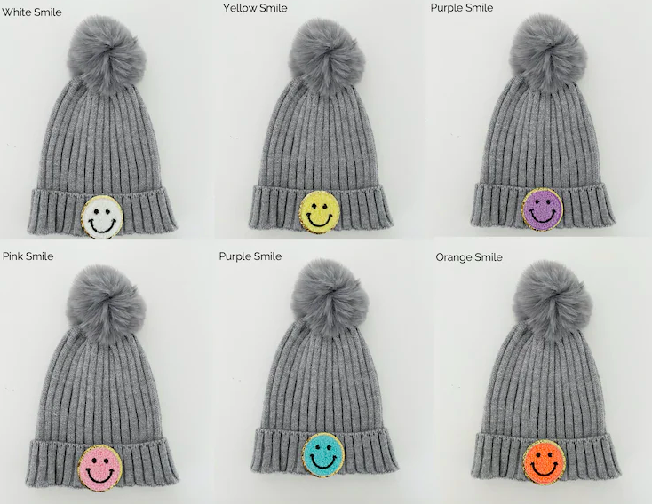 six grey knit beanies with a grey pom pom at the top and a smiley face patch in different colors per beanie on the front