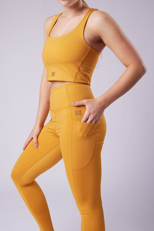 A model wearing gold-colored high-waisted leggings with pockets and a matching crop top
