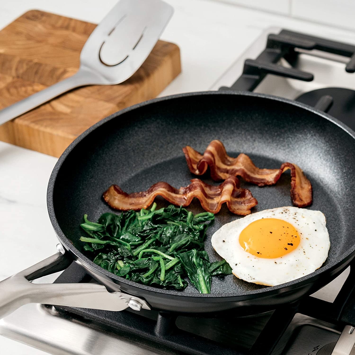A frying pan with bacon spinach and an egg in it