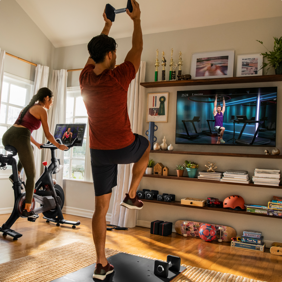 one person on a peloton bike and the other person doing floor exercises watching peloton workouts on the tv