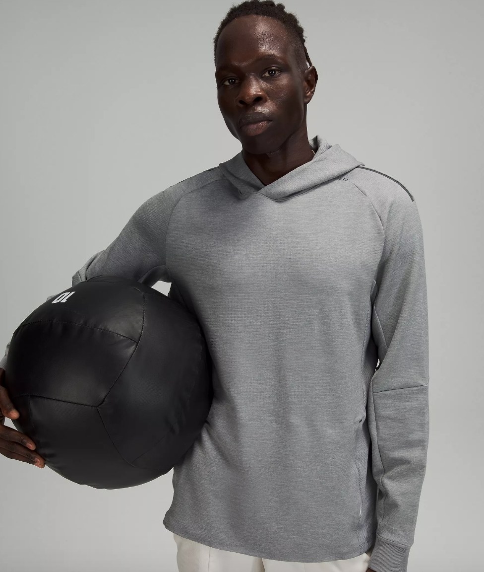 Model wearing gray sweatshirt holding black workout ball