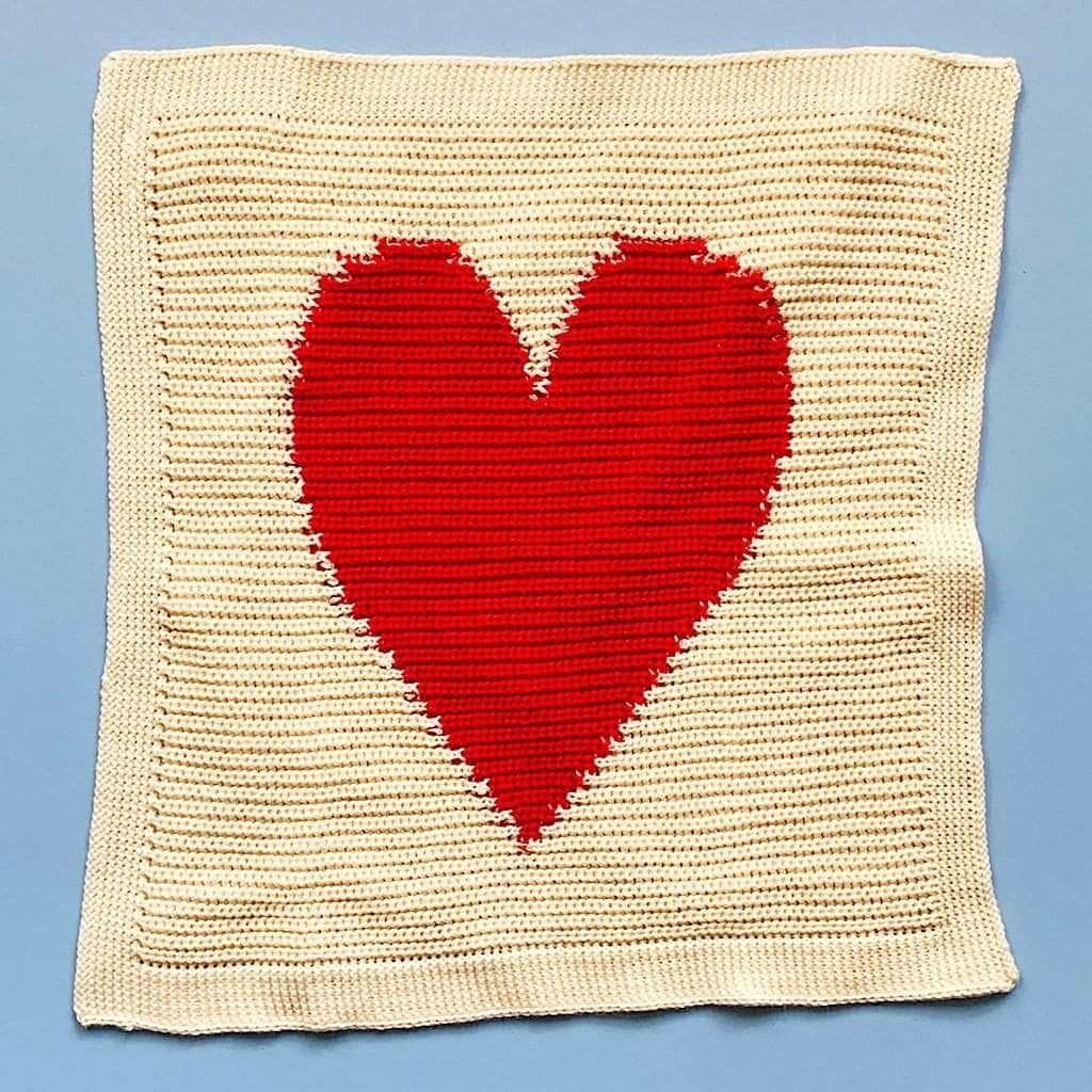 A cream colored baby blanket with one large red heart in the middle
